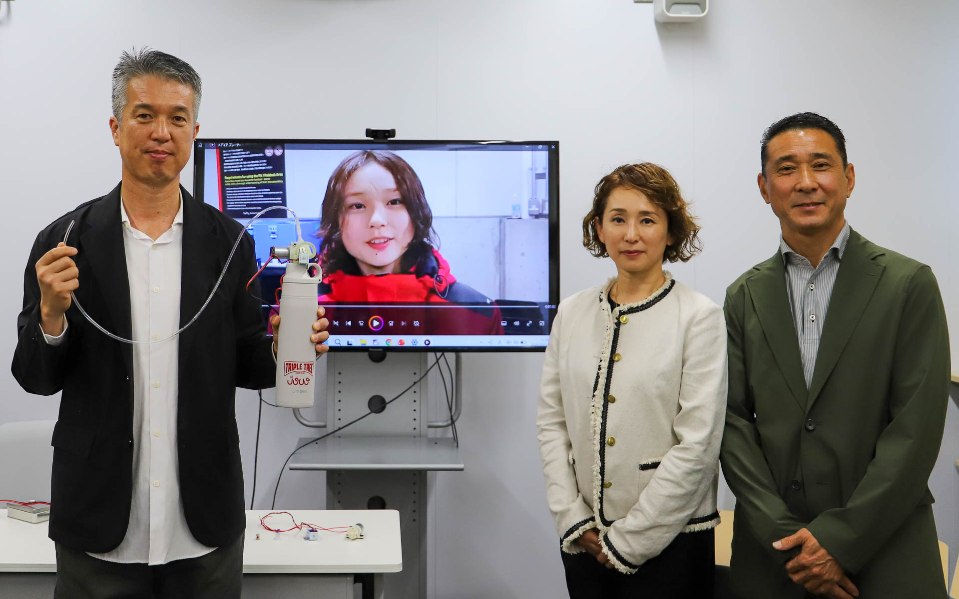 タイガー魔法瓶がJuju選手のために開発したドリンクシステム「Cool-Flow HYDRATION」の説明会が開かれた。左からタイガー魔法瓶株式会社 R＆Dマーケティンググループの村田勝則氏、NODAレーシングコンサルタンツの野田雅恵氏と野田英樹氏。ディスプレイに映っているのがJuju（野田樹潤）選手
