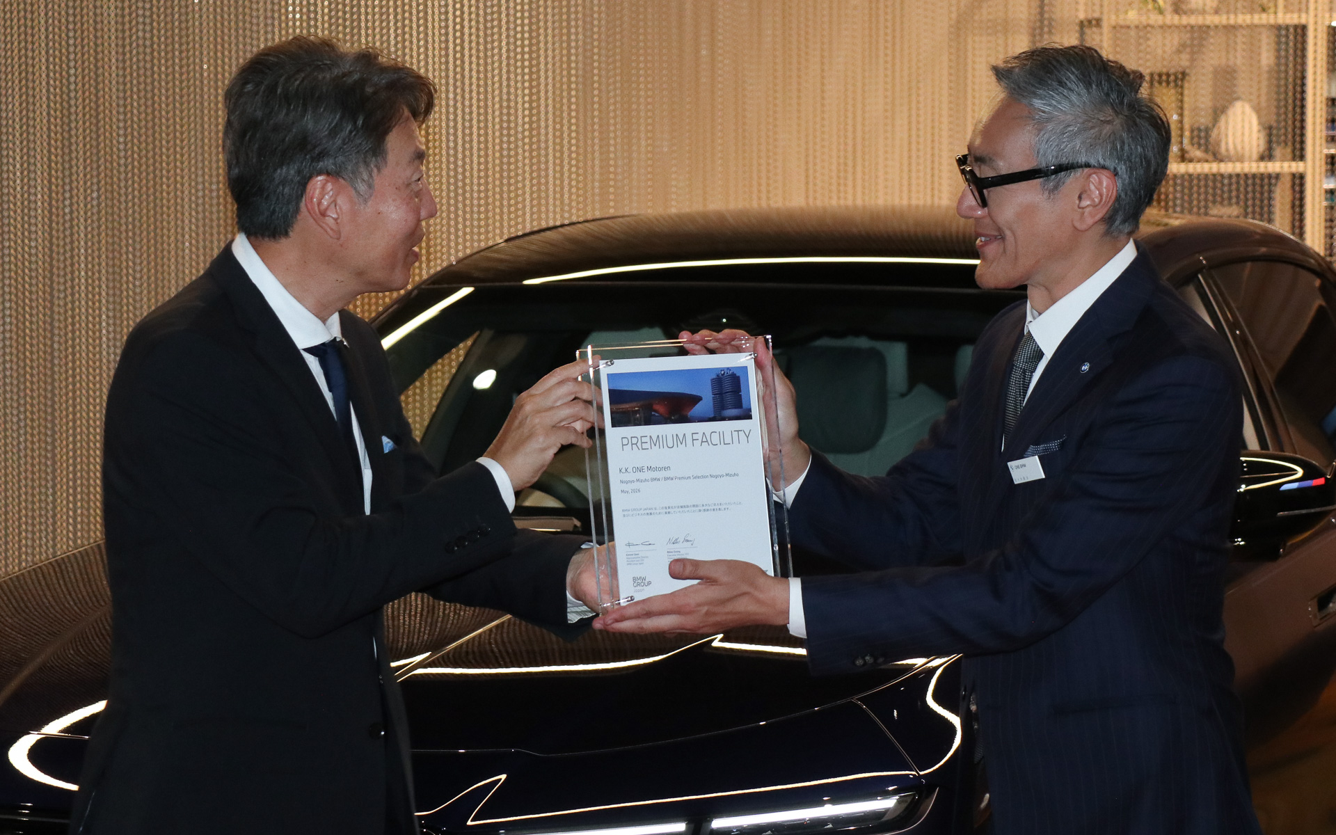 レセプションパーティではビー・エム・ダブリュー株式会社 代表取締役社長 上野金太郎氏（左）から株式会社ONE モトーレン 代表取締役社長 佐々木鋭治氏（右）に感謝の意を込めたウルクンデ（ドイツ語で証明書、認定証などの意味）も手渡された