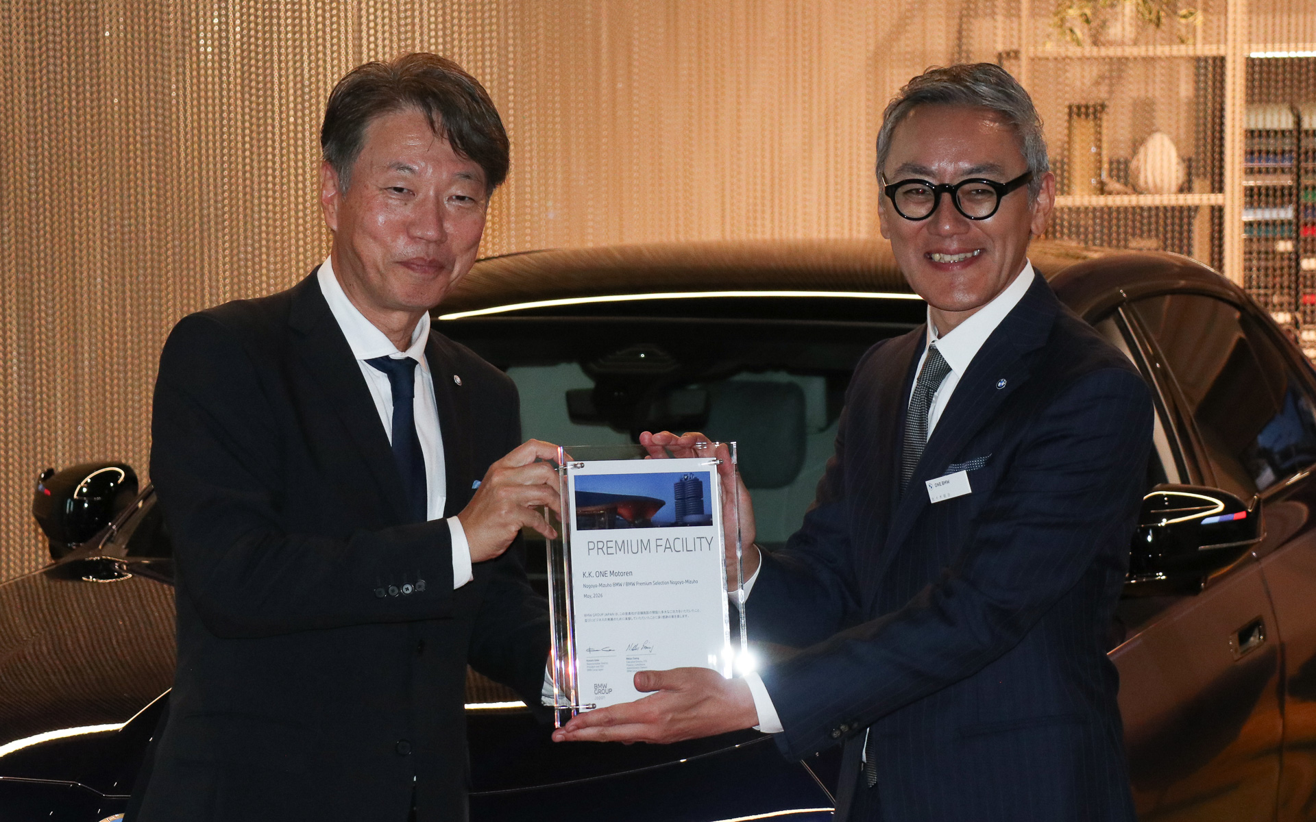 レセプションパーティではビー・エム・ダブリュー株式会社 代表取締役社長 上野金太郎氏（左）から株式会社ONE モトーレン 代表取締役社長 佐々木鋭治氏（右）に感謝の意を込めたウルクンデ（ドイツ語で証明書、認定証などの意味）も手渡された