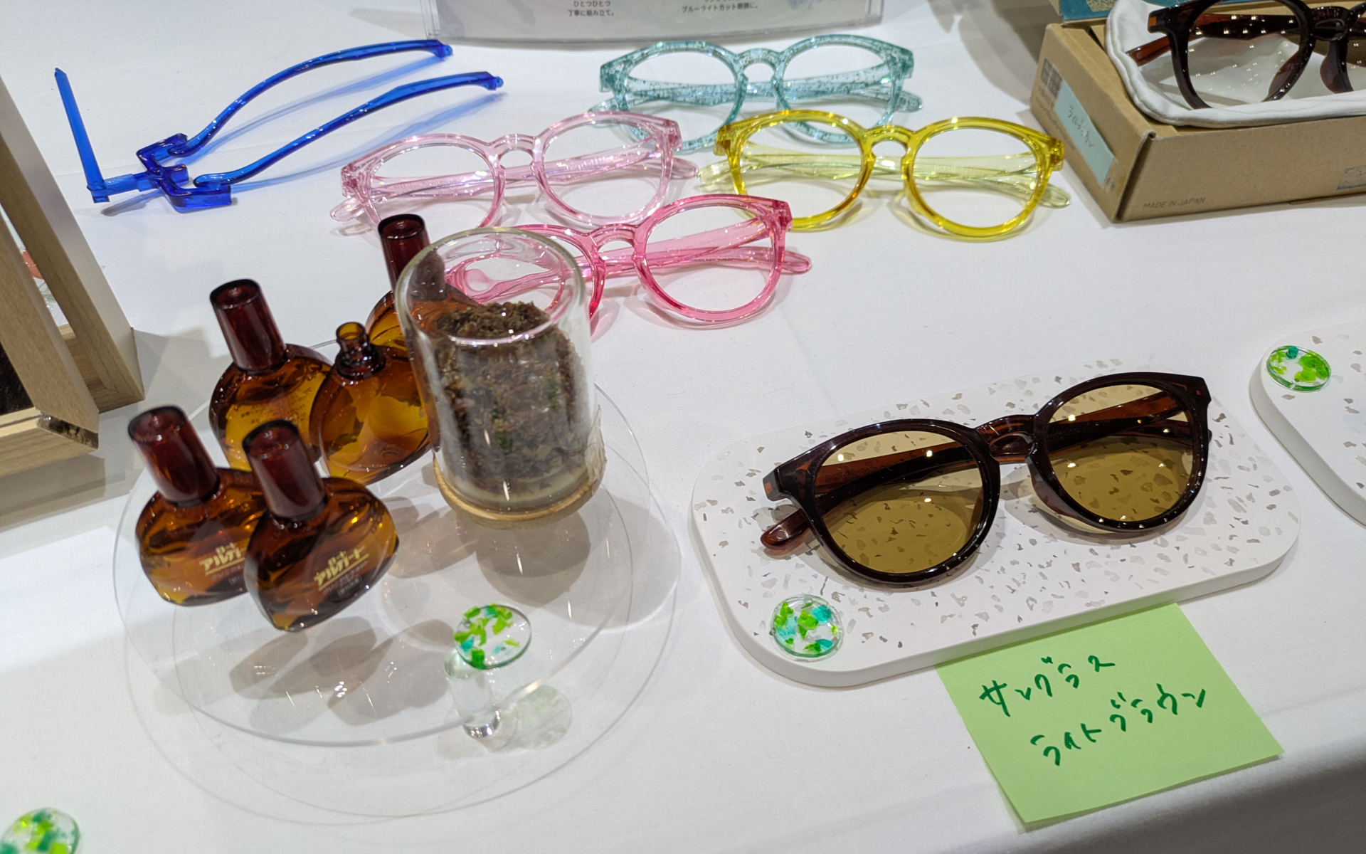 ロート製薬の社内ベンチャーから生まれたアイフォースリー（eyeforthree）は、目薬ボトルの廃プラスチックを再利用して作られた、サングラスや小物（試作品）を展示。目薬のボトルは安全性のため再生材は使用できない。そのため製造過程で廃材になったプラスチックがゴミとなっていたことからサングラス作りが誕生したという。サングラスの価格は1万5000円