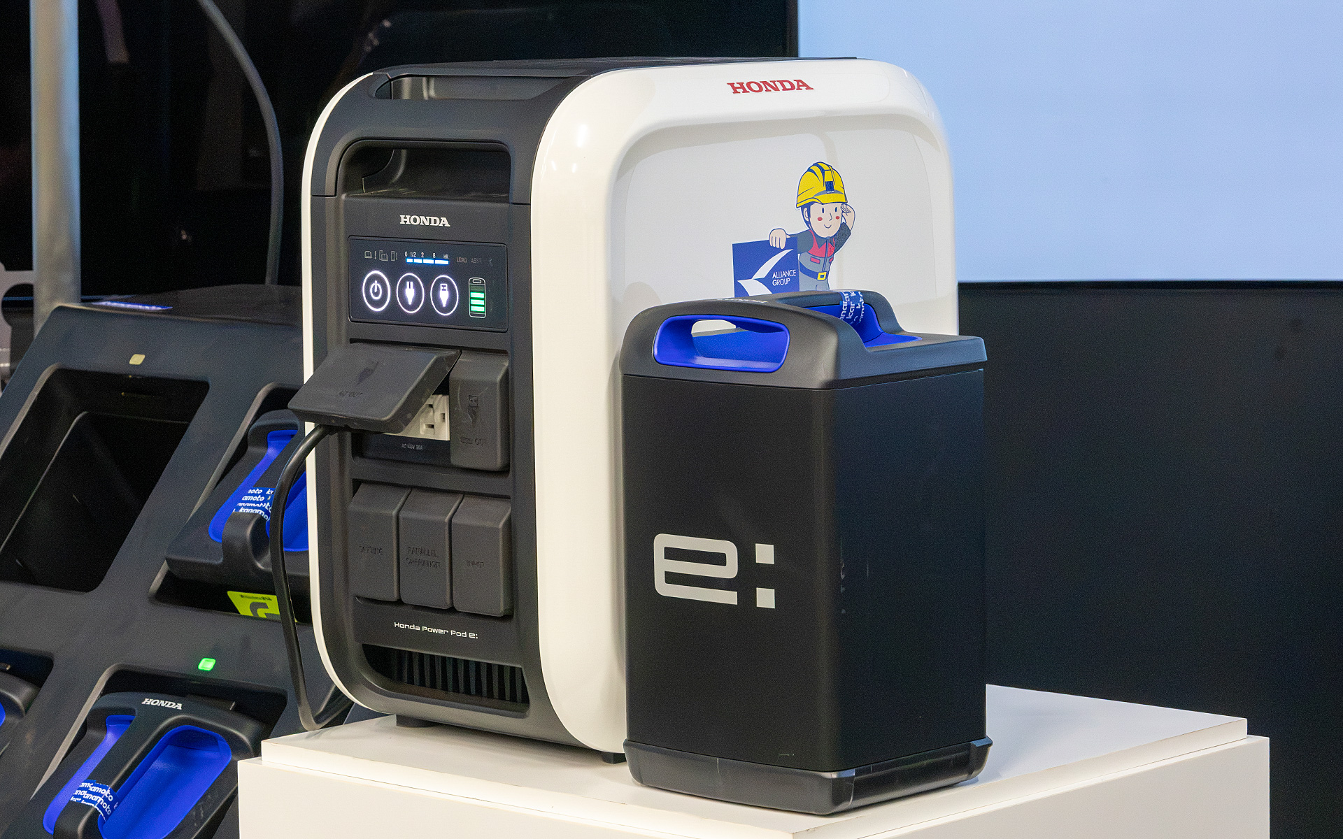 手前の黒いものが、ホンダの交換式バッテリ「Honda Mobile Power Pack e:（ホンダ モバイルパワーパック イー）」。奥にあるのはモバイルパワーパック イーの電気を取り出して、外部と接続できるようにする「Honda PowerPod e:（ホンダ パワーポッド イー）」