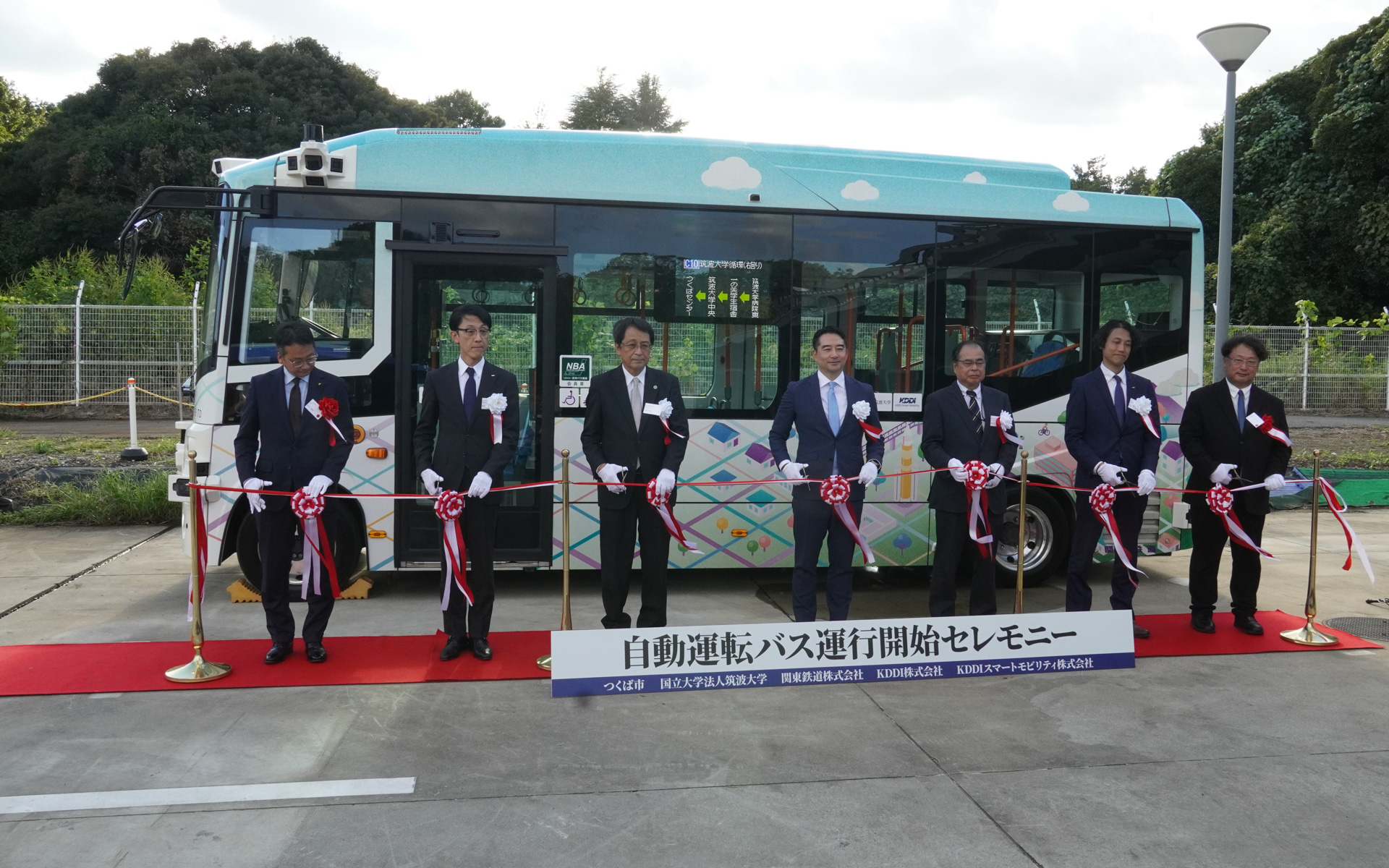 運行開始セレモニーでテープカット。左からつくば市議会議長の黒田健祐氏、KDDI株式会社 取締役執行役員常務の勝木朋彦氏、国立大学法人 筑波大学長の永田恭介氏、つくば市長の五十嵐立青氏、関東鉄道株式会社 代表取締役社長の登嶋進氏、KDDIスマートモビリティ株式会社 代表取締役社長の松田慧氏、デジタル庁 国民向けサービスグループ審議官の佐野究一郎氏