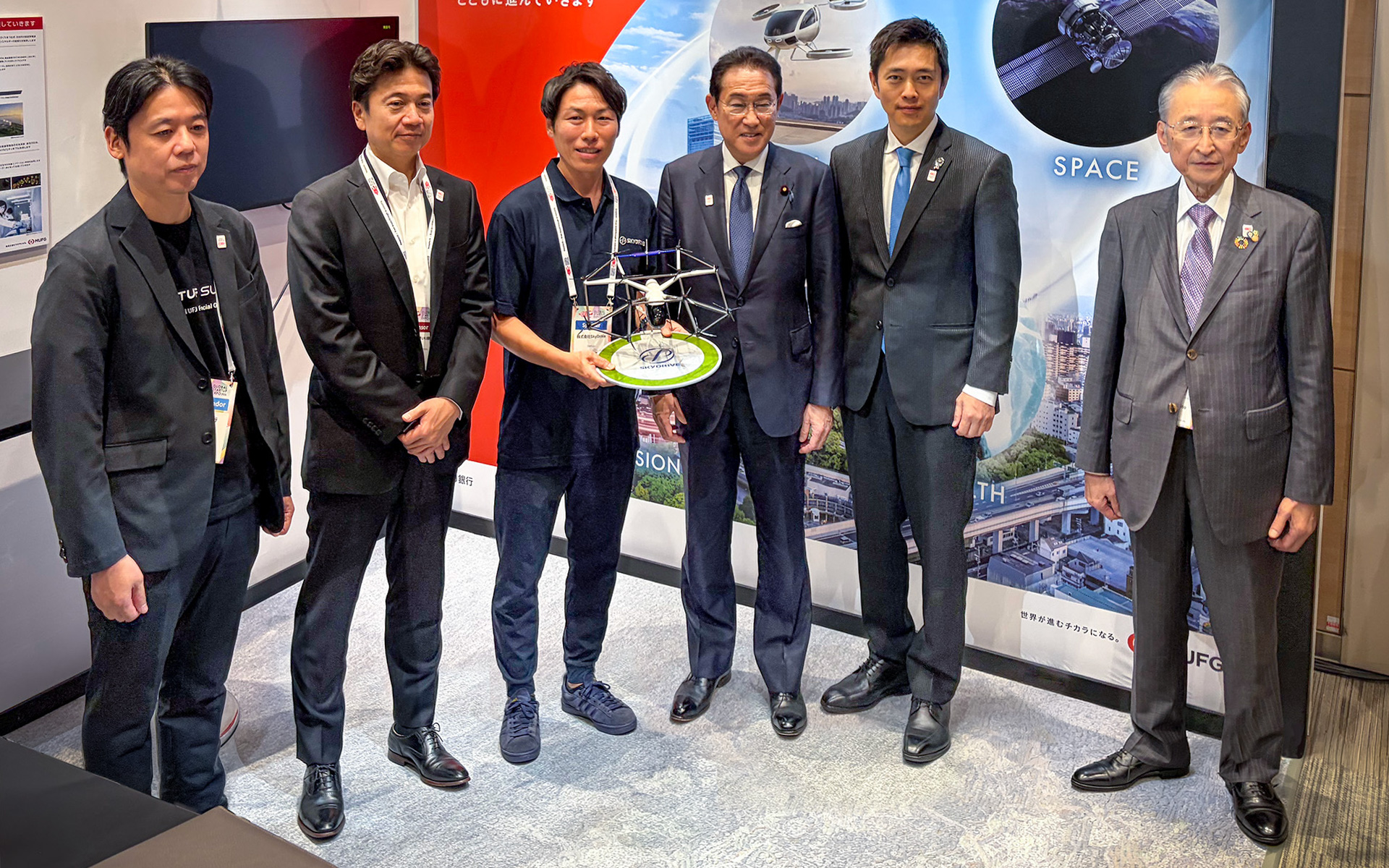 大阪で実施されている「Global Startup EXPO 2026」の三菱UFJ銀行ブース。写真左から、三菱UFJ銀行 スタートアップ戦略部長 西地賢祐 氏、三菱UFJ銀行 取締役専務執行役員（代表取締役）西日本駐在 北村慎氏、SkyDrive 執行役員 グローバル事業統括責任者 小野泰司氏、岸田文雄元首相、大阪府 吉村洋文知事、NEDO 理事長 斎藤保氏（写真提供：SkyDrive）