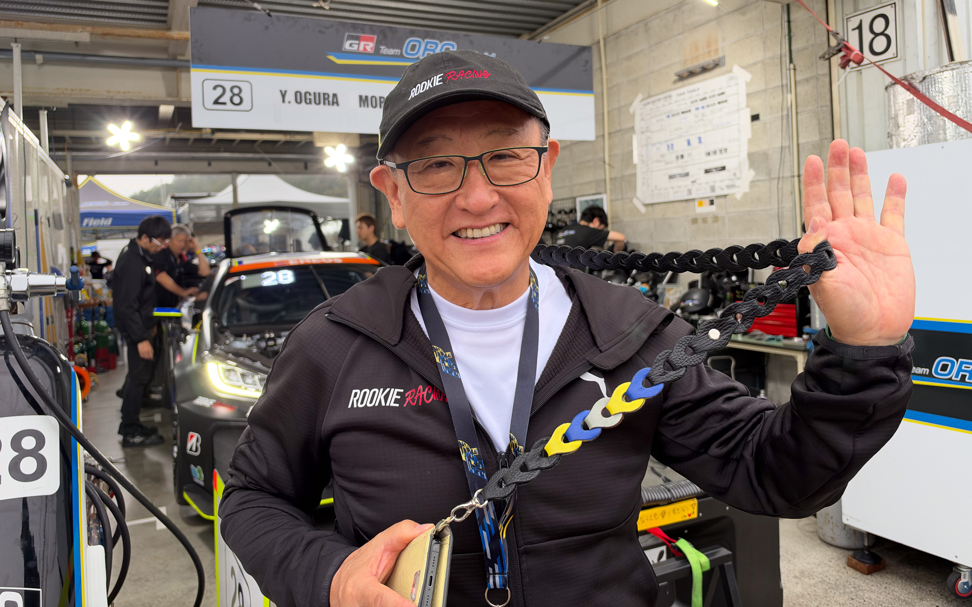 ルーキーレーシングカラーがワンポイントに入ったアップサイクルスマホストラップを身に着けるトヨタ自動車株式会社 代表取締役会長 豊田章男氏。第6戦岡山ではGR Team ORC Fieldのモリゾウ選手として参加