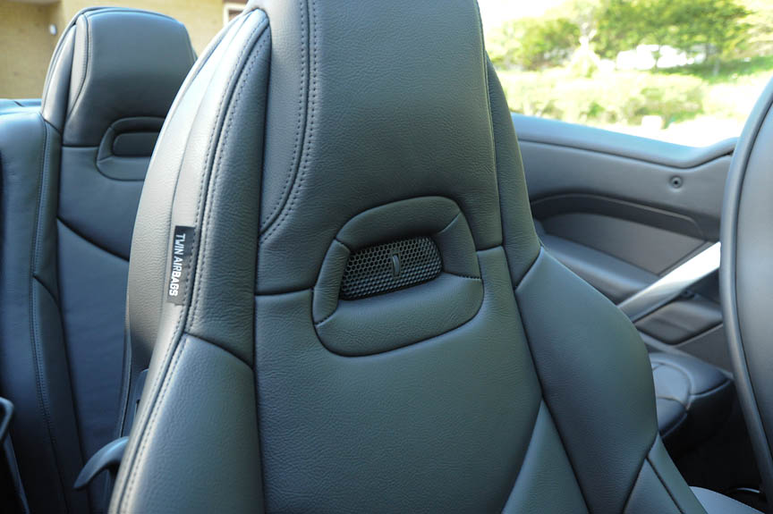 フロントシートのヘッドレスト下には「ネックウォーマー」を標準装備（写真右）。ここから温風が吹き出し、オープン時のドライブを快適にする。方向と温度（風量）は3段階で変更でき、メインのエアコンとは独立して制御できる。シフトレバーの後ろにコントロールスイッチがある