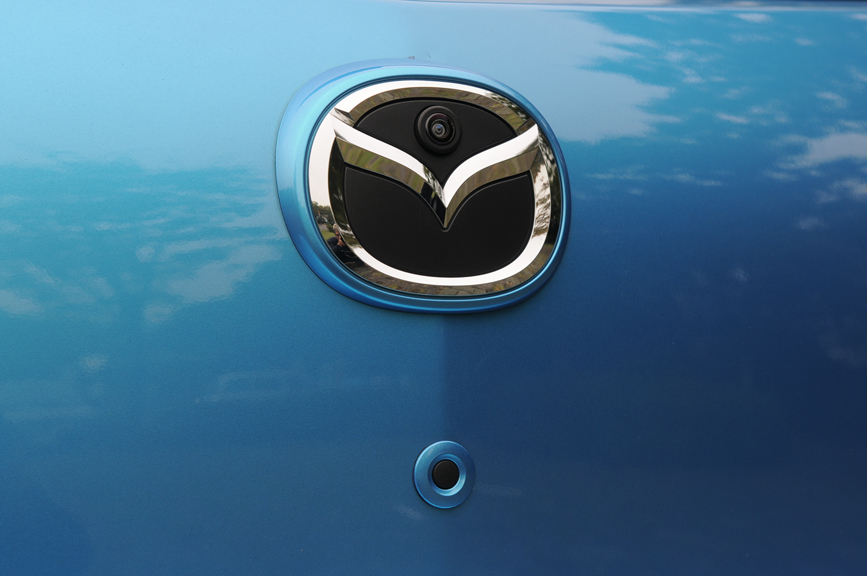 リアのマツダロゴにはバックカメラが内蔵されている。遠目にはカメラが目立たないのでシンプルに見える。下はリアハッチのオープンボタン