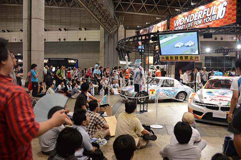 グッドスマイルカンパニーブースの一角に用意されたデモ車輌の展示とパブリックビューイングのコーナー。応援グッズを身につけ小旗を振ってモニターに見入る人も少なくない
