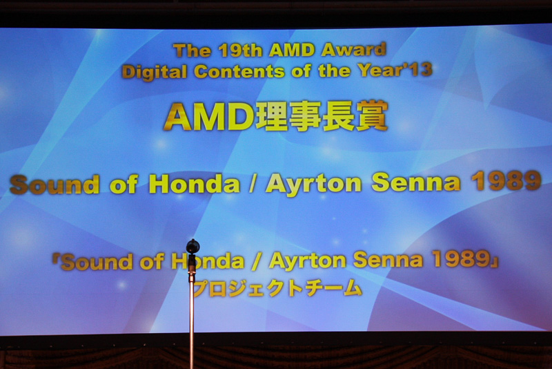 デジタルメディア協会 理事長の襟川惠子氏から本田技研工業 インターナビ事業室の三河昭広氏に、AMD理事長賞の表彰状とモノリスが贈られた