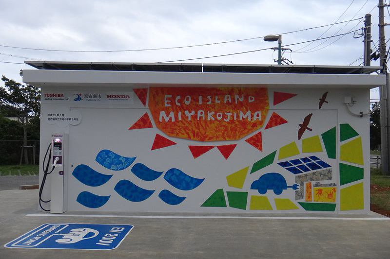 下地庁舎のPV充電ステーション。壁面の絵は宮古島市立下地小学校の6年生の手によるもの。MC-βは「走る姿がカワイイ」という感想が圧倒的に多く、下地小学校の生徒のみんなから愛されていた