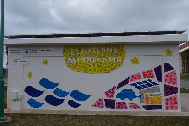 下地庁舎のPV充電ステーション。壁面の絵は宮古島市立下地小学校の6年生の手によるもの。MC-βは「走る姿がカワイイ」という感想が圧倒的に多く、下地小学校の生徒のみんなから愛されていた