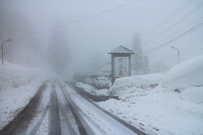 関温泉入り口。まだ冬の始まりなので、道路にはアスファルトが見えている。が、両脇に積み上げられた雪は既に1.5mを超えている