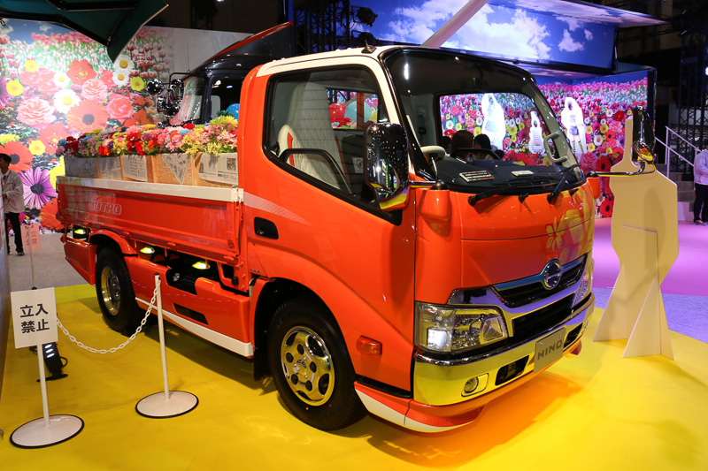 デュトロ ハイブリッド カーゴのボディパネルはメタリックオレンジをベースに、ルーフや荷台パネル、バンパーなどに白いアクセントを設定。車内にはキルティング加工の白い革張りシートを採用する