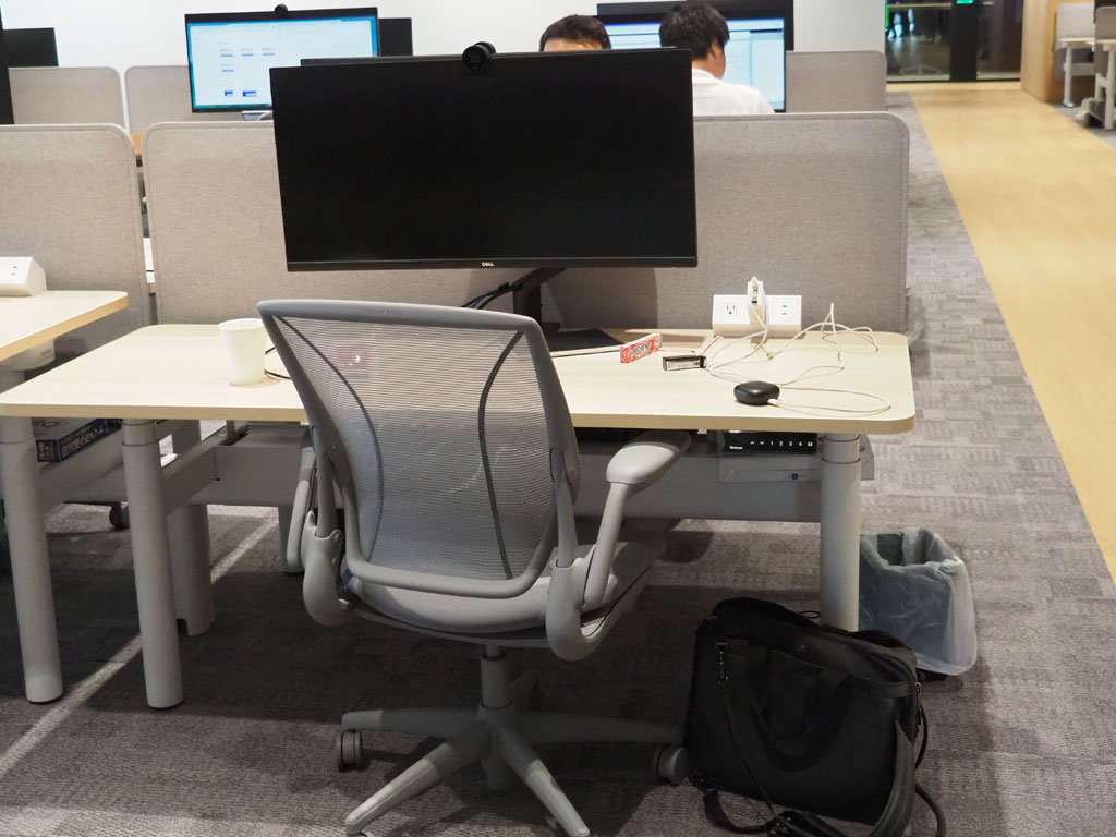 社員のデスクはフリーアドレス。昇降式のデスクで、デスクの下には防災対策としてヘルメッドが用意されている