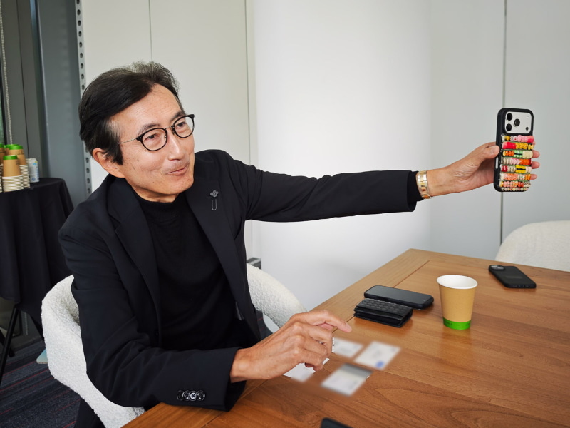 Salesforceのマーク・ベニオフCEOとおそろいだという寿司のミニチュアがついているスマートフォンケースを見せる小出氏。ベニオフCEOは禅の文化に精通し、日本に滞在する時は京都で座禅を組むなど、日本通としても知られている