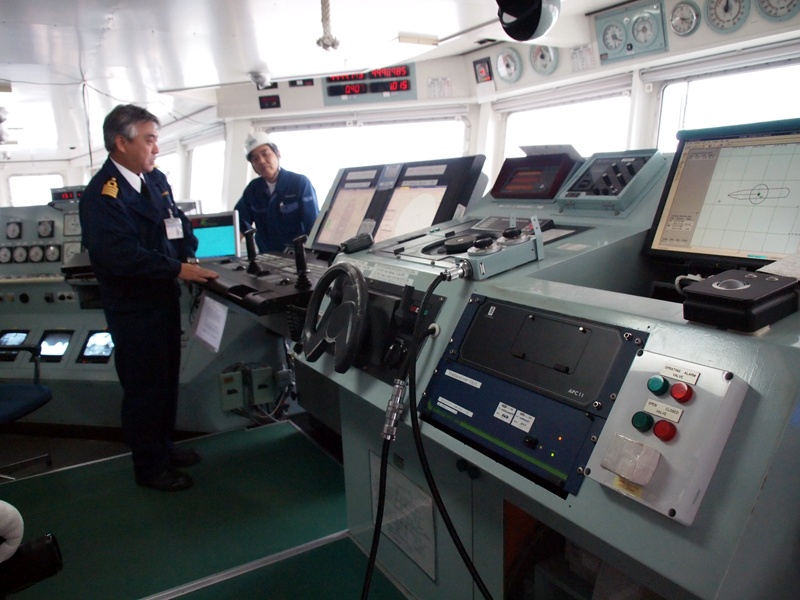 手前が舵、奥がDPS。説明しているのは鈴木昭一船長。