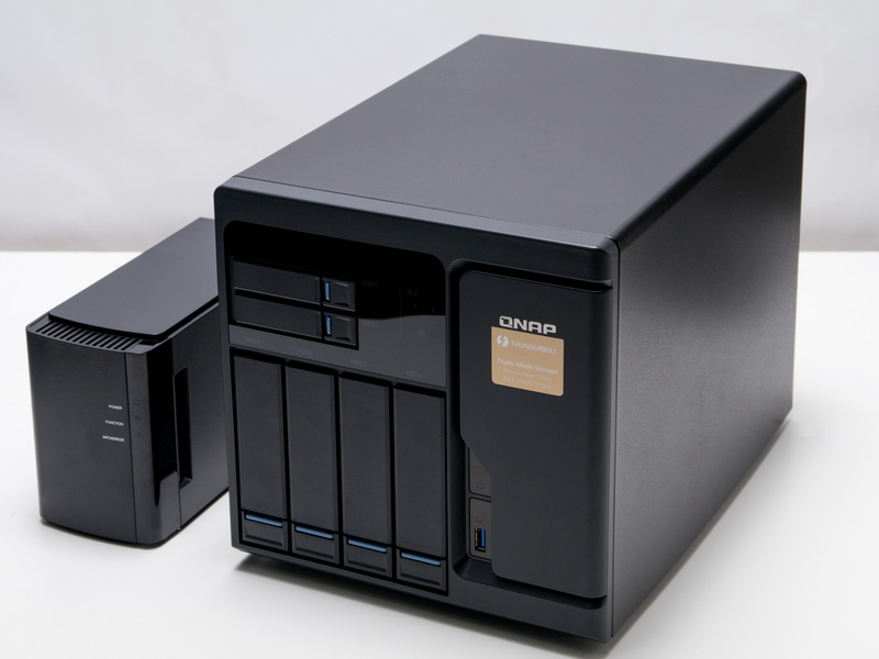 化粧箱から取り出した「TVS-682T」。外形寸法はH 231.9×W 224.9×D 319.8mmと小型のパソコン並みの大きさ。デスクの上に置くにはちょっと大きい。本体のみで7.7kg（HDD、SSD含まず）とずっしりなので、しっかりとしたラックなどに設置したい。ちなみに横にあるのはこれまで筆者が使用していた国産メーカーのNAS。