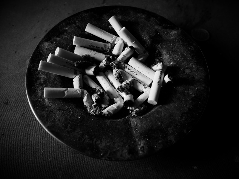 年季が入った灰皿と無造作に捨てられた吸い殻。光の当たり方でいつもの灰皿が違って見える。周辺の光量を落とすことで、中央の被写体を強調した。<br><span class="fnt-85">オリンパス PEN-F / M.ZUIKO DIGITAL 17mm F1.8 / 17mm（34mm相当） /  マニュアル露出（F4、1/25秒） / ISO 200/ WB:オート</span>