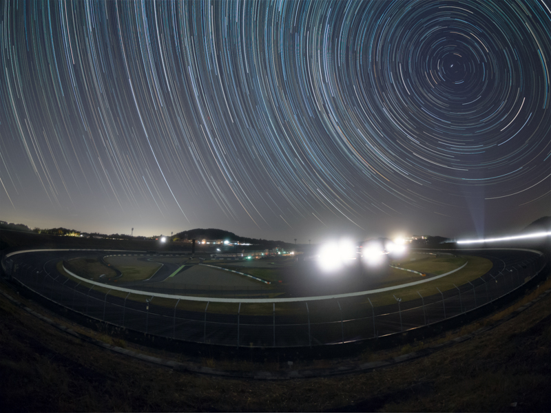 スーパースピードウェイのターン1と2の中間あたりからフィッシュアイレンズで撮影したコース全景と星の日周運動。ときどき何かの作業で短時間照明がついたが、ほとんどの時間は邪魔な光が無く撮影ができた。まぁ少々の灯りがあっても、かえってこういう場所らしい雰囲気になる。<br>OLYMPUS OM-D E-M5 Mark II／M.ZUIKO DIGITAL ED 8mm F1.8 Fisheye PRO／ISO1600／F2／8秒設定でライブコンポジット撮影約2.5時間／LEEソフトフィルターNo.3使用