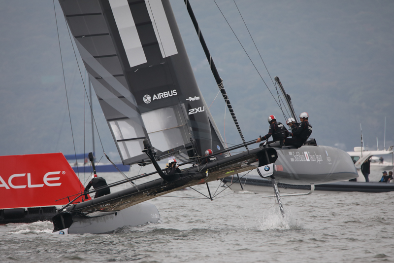 大きく風を受け、ラダー（舵板）が浮くほど船体を傾けカーブを曲がる。船艇に逆L字となったダガーボードが見える。船尾中央付近に座りクルーにカメラを向けているのはゲスト。<br><span class="fnt-85">EOS 5D Mark IV・SP 150-600mm F/5-6.3 Di VC USD G2・1/1250秒・F8.0・−2/3EV・ISO800・絞り優先AE・600mm・RAW（DPPにてJPEGに生成）</span>