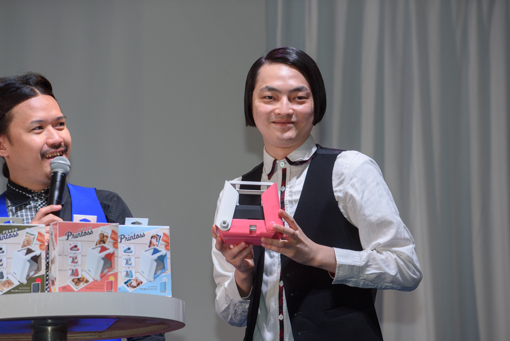 筧さんが気に入ったという「SAKURA」カラーのプリントスを手に、すましたポーズで笑いをとるピスタチオの小澤慎一朗さん。