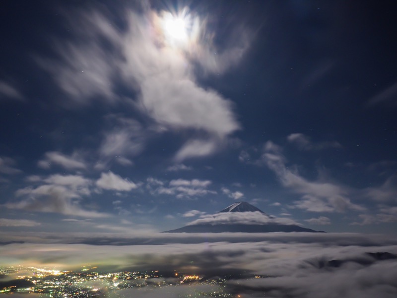 夜の新道峠より。月明かりに浮かぶ富士山の姿は、肉眼でも美しいと感じる。雨上がりの雲海を期待して待機していると、何やら様々な雲が現れ始め、夜の景色を華やかにしてくれた。富士山の頭上に現れた雲のおかけで、印象的な1枚に仕上がった。<br><span class="fnt-85">OLYMPUS OM-D E-M1 Mark II / M.ZUIKO DIGITAL ED 12-100mm F4.0 IS PRO / 14mm（28mm相当） / マニュアル露出（F11、60秒） / ISO 400</span>