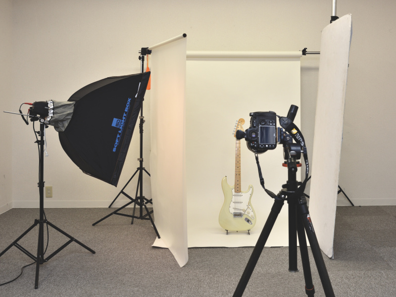 壁からギターの手前まで伸ばした白い背景紙をベースに、左サイドに設置したソフトボックス・ライトの前方にディフューザーを垂らし、右サイドにはレフ板を置いています（写真は上の白ストラト撮影時のもの）。