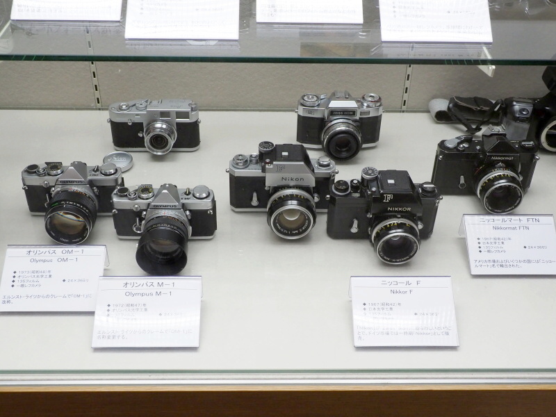 オリンパスOM-1とニコンFは、それぞれ「M-1」と「Nikon」に他社からクレームがつき、名称変更した経緯がある。背後に並ぶカメラは……