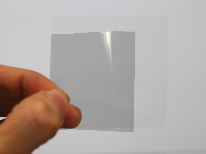 手前に位相差板、奥に偏光板をかざしている。光源はノートPCのディスプレイ。偏光板そのもののグレーが見えている。