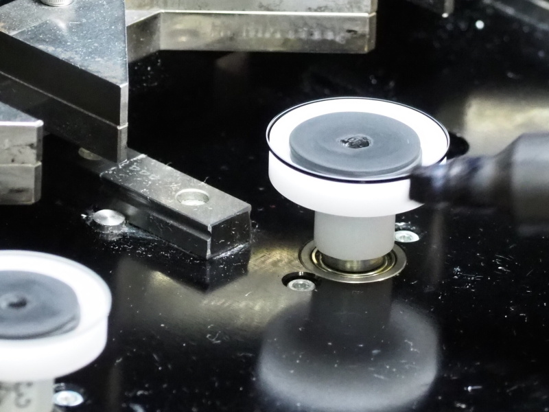 ガラスを吸着・回転させレンズ外周部に墨塗り処理を行う。