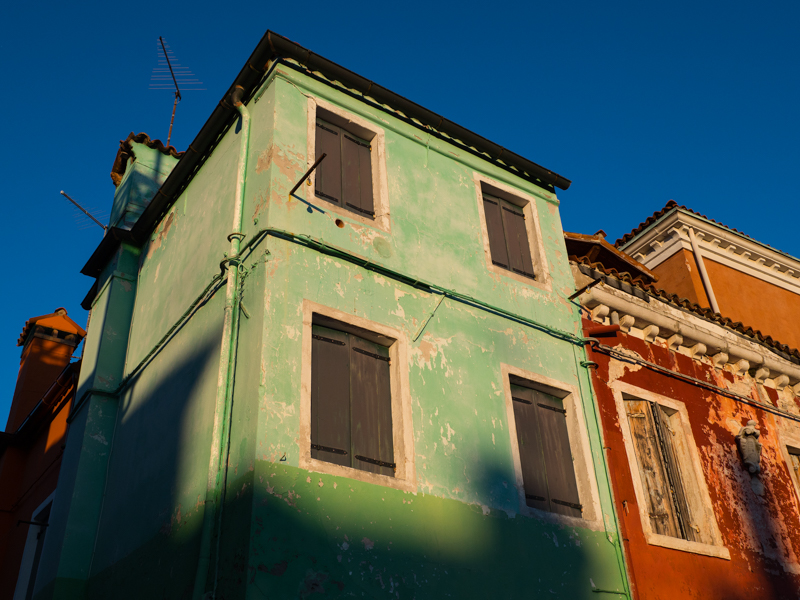本島から荒波に揺られ乗り継いでたどり着いたブラーノ島にて。建物が渋い感じに経年していたので午後の光線で浮き上がらせた。開放F値も良いが絞り込むと解像度が一気に増す。<br><span class="fnt-85">OLIMPUS OM-D E-M1 Mark II / M.ZUIKO DIGITAL ED 17mm F1.2 PRO / 17mm（34mm相当） / 絞り優先AE（F6.7、1/500秒、±0EV） / ISO 200</span>