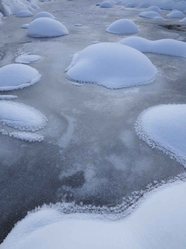 厳寒の朝に川が凍結し、氷の上には珍しいフロストフラワーが発生していた。氷と岩に積もった雪をデザイン的に表現するためカメラアングルを低くしている。<br><span class="fnt-85">OLYMPUS OM-D E-M1 Mark II / M.ZUIKO DIGITAL ED 7-14mm F2.8 PRO / 12mm（24mm相当） / 絞り優先AE（F22、1/100秒、±0EV） / ISO 400</span>