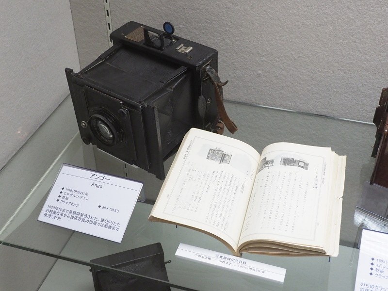 ドイツ・C.P.ゲルツの「アンゴー」（1896年）。1920年代まで長期間製造されたクラップカメラ。薄く折りたためて軽量なため、報道写真の現場で戦後まで使用された。80×105mm乾板。手前は小西本店の「写真機械用品目録」。