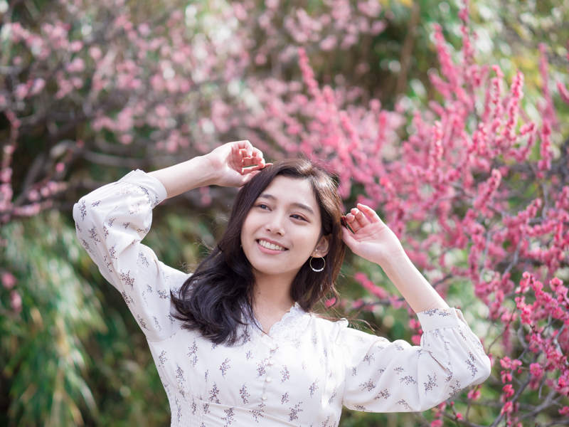 ピンク色の梅の花の前でリラックスしているモデルの表情が良いと思ったのでシャッターを切った。適度な背景描写が、嫌味なく情景を説明している。<br><span class="fnt-85">OLYMPUS OM-D E-M1 Mark II / 45mm（90mm相当） / マニュアル露出（F1.4、1/4,000秒） / ISO 200</span>