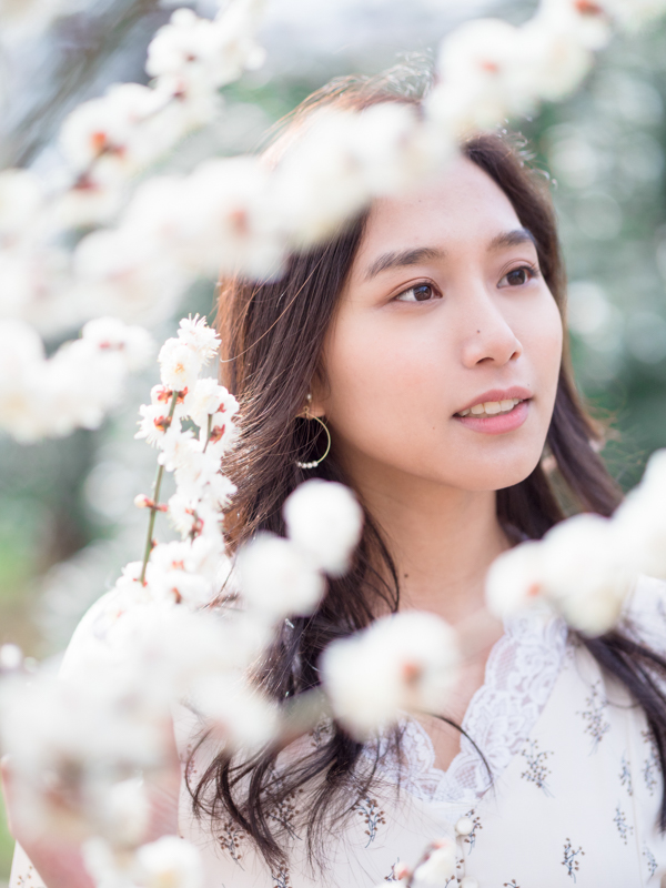 白い梅を観賞する姿を撮影。風でモデルの前にある梅の花が大きく揺れていたが、瞳優先AFのおかげでストレスなく被写体の瞳にピントを合わせられた。<br><span class="fnt-85">OLYMPUS OM-D E-M1 Mark II / 45mm（90mm相当） / マニュアル露出（F1.2、1/5,000秒） / ISO 200</span>
