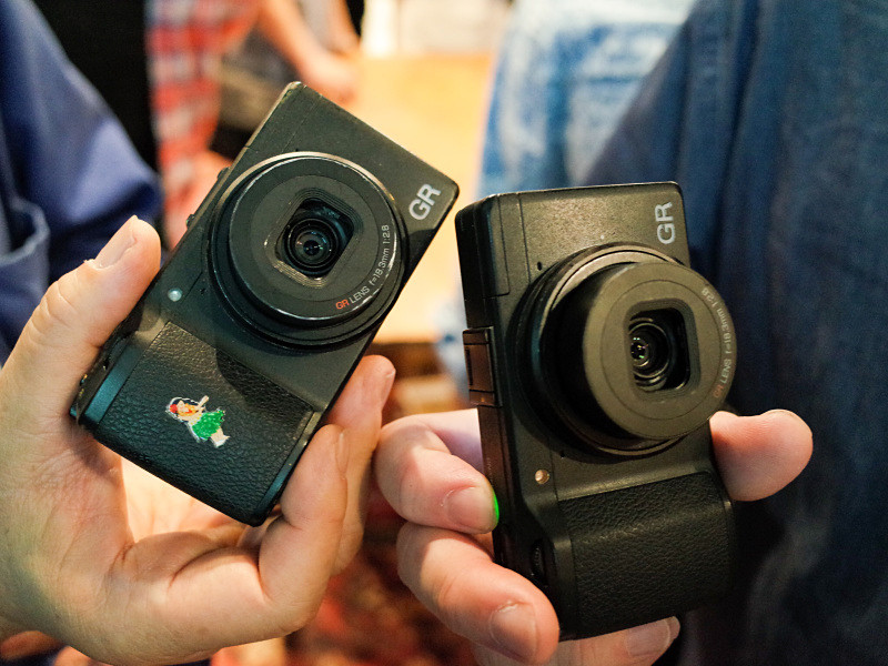 左から、田中長徳さんと中藤毅彦さんのGR（2013年モデル）。中藤さんは右手親指にネックストラップを巻きつけて持ち、田中長徳さんは"ストラップレス・アナーキスト"を貫く。