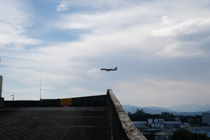 少しでも瑞穂町を俯瞰で見ようと、モールの3階駐車場に上がって眺めていると、飛行機が飛んで来た。かなり近い。低空飛行だ。向かう先は横田基地か……<br><span class="fnt-85">X-Pro2 / XF35mmF1.4 R / 35mm（53mm相当） / 絞り優先AE（1/750秒・F8・+0.3EV） / ISO 200</span>