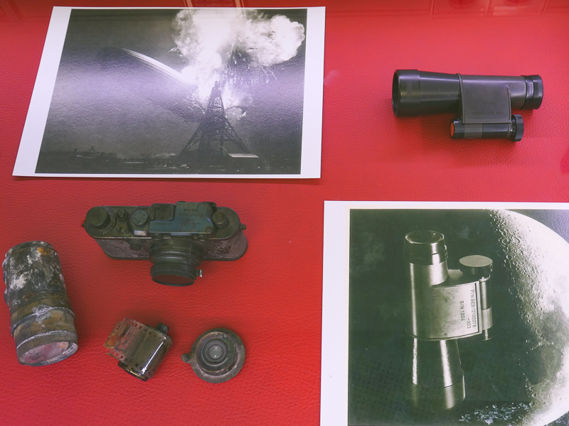 左は1937年のヒンデンブルク号爆発炎上事故現場から出てきたライカ。右はアポロ11号で宇宙へ行った双眼鏡（省スペース化のために片眼側だけ使った）。NASAの厳重なナンバリングが特徴的。