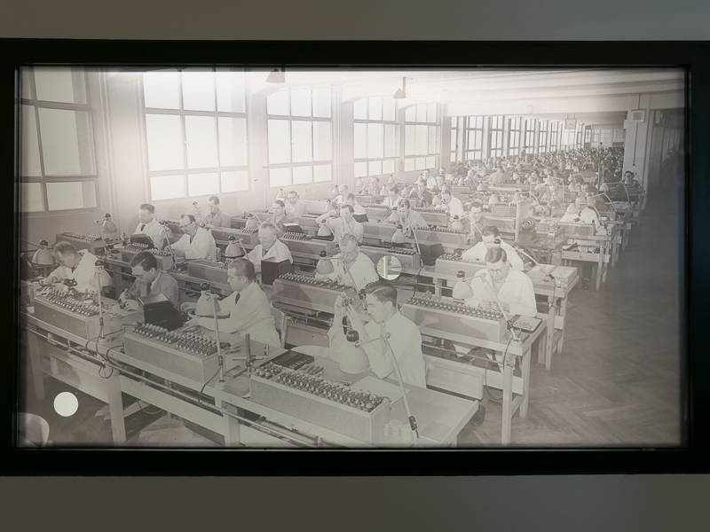 壁に大きな写真。1930年代と見られるライカ組立工場の様子。中央と左下に穴が見える。