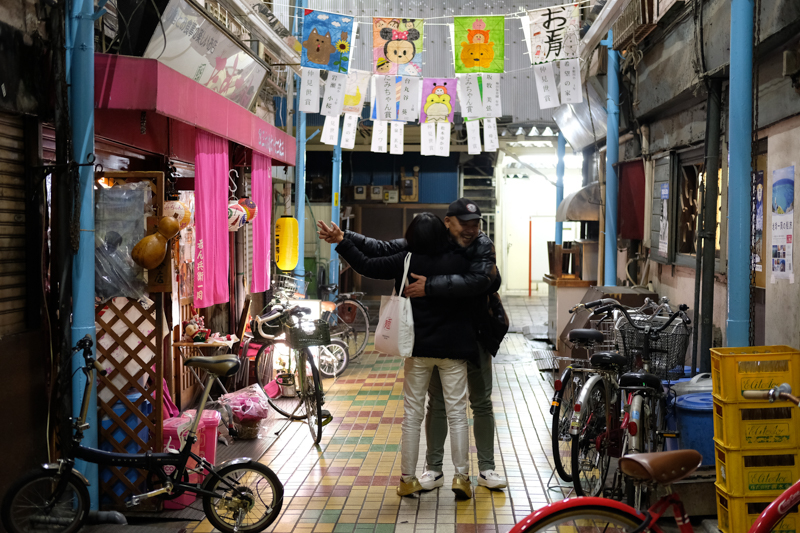 一緒に飲んでいた知り合いの女性が店を出た途端、知ってるおじさんと出会って抱きあうの図。人と人が近しい街なのだ。<br><span class="fnt-85">X-E3 / XF35mmF2 R WR / 35mm（52.5mm相当） / 絞り優先AE（1/30秒・F2.0・+0.7EV） / ISO 1600</span>