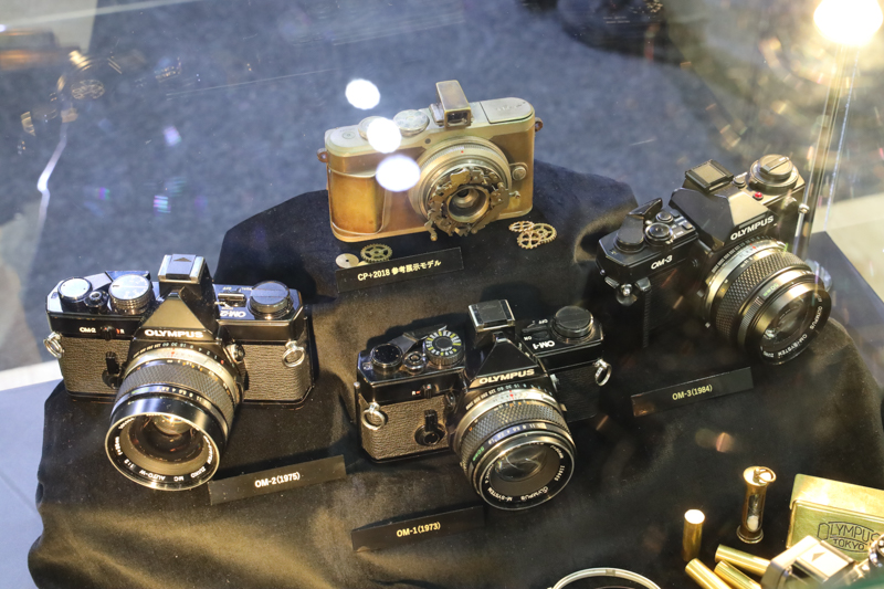 歴代のフィルムOMシリーズと、CP+2018で参考展示されたスチームパンクなPENデジタル（上）。