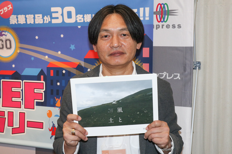 岡嶋和幸さん。写真集「風と土 Wind and Earth」を手に。
