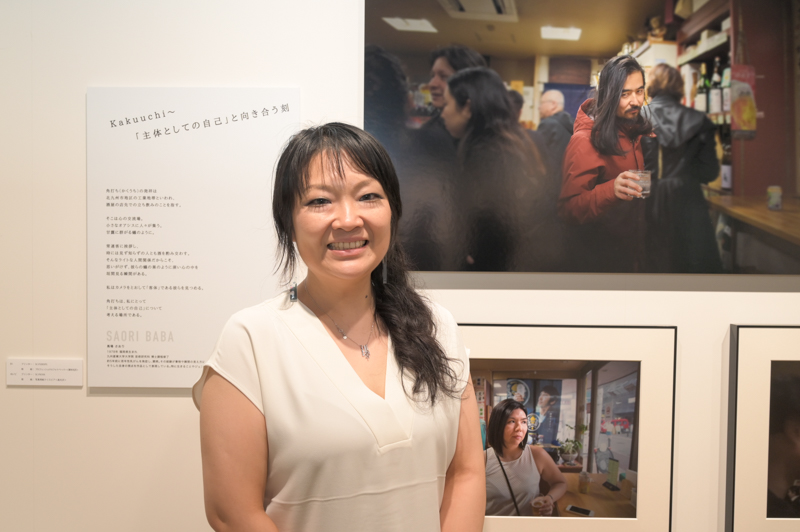 馬場さおりさん。エキシビジョンの作品「kakuuchi〜『主体としての自己』と向き合う刻」の前で。人物にフォーカスしたという点では共通しているものの、主要な被写体以外を暗く落とし込み、人物をスポットで浮かびあげる手法を見せた