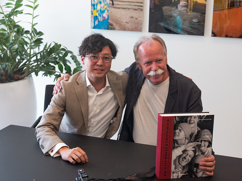 本展図録に寄稿した写真史家の打林俊氏（左）と、キュレーターのハンス・コエッツル氏。手にしている図録には約1,000点の作品が掲載されている。