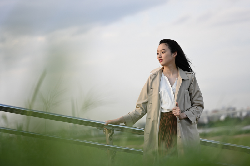 草むらの中に寝転ぶような姿勢で、前ボケを生かしながらモデルを撮影した。なだらかで自然な前後のボケに挟まれた被写体は、Z 7の瞳AFによる的確な結像性能も相まって、とてもシャープに描写されている。秋の風を感じる奥行きのある1枚に仕上がった。<br><span class="fnt-85">ニコン Z 7/ NIKKOR Z 85mm f/1.8 S / 85mm / マニュアル露出（F1.8、1/1,250秒） / ISO 100</span>