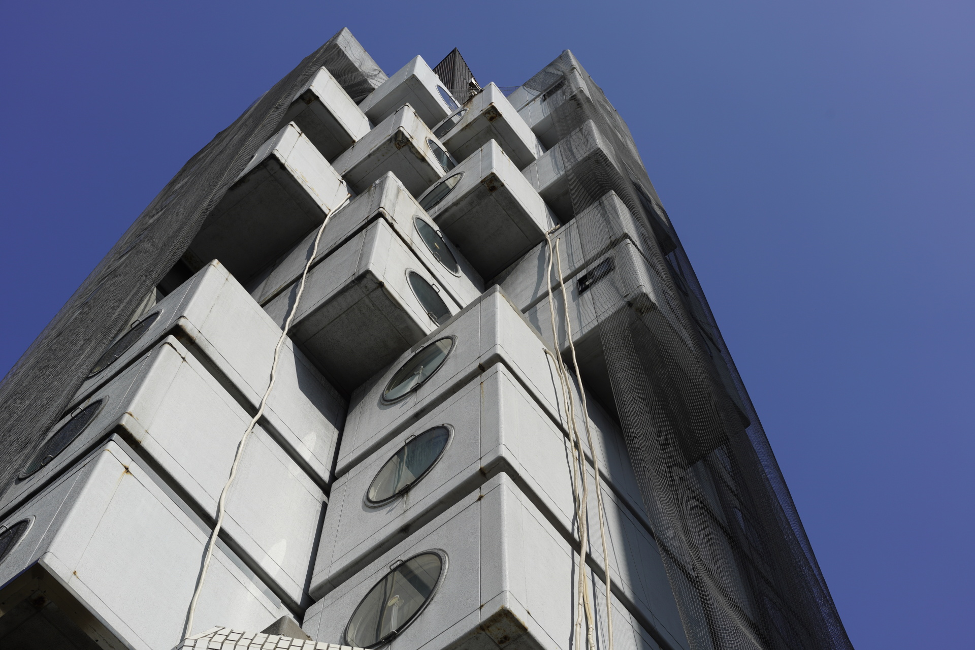 前を通りかかるといつも見上げてしまう、有名なカプセル型マンション。写真に捉えて観察すると、経年変化の様子が細部まで確認できた。掛けられたネットの描写も、線が細く自然なシャープさで、その柔らかな質感が伝わってくる。<br>α7R IV　APO-LANTHAR 50mm F2 Aspherical E-mount　ISO 100　F8　1/500秒