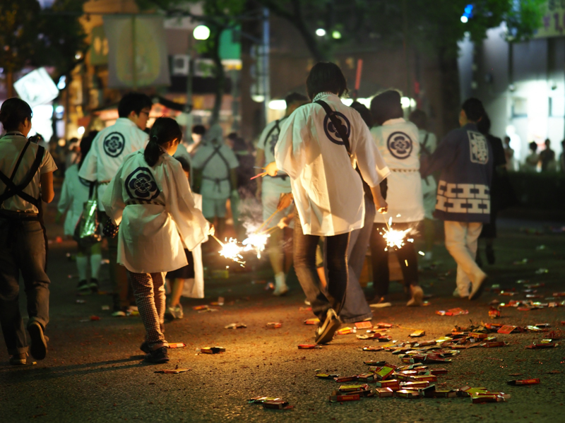 お盆には故人を送る精霊船を曳いて海までいく。その道中は大量の花火や爆竹で賑やかだ。その様子を大口径F1.2のレンズは暗くなった時間の行事を浮かび上がらせていく。少し望遠になり人々や花火から離れて撮影できる程よい距離感もいい（撮影：斎藤巧一郎）。<br><span class="fnt-85">OLYMPUS OM-D E-M1 Mark II / M.ZUIKO DIGITAL ED 45mm F1.2 PRO / 45mm（90mm相当） / 絞り優先AE（F1.2、1/50秒、±0EV） / ISO 800 / WB：オート</span>