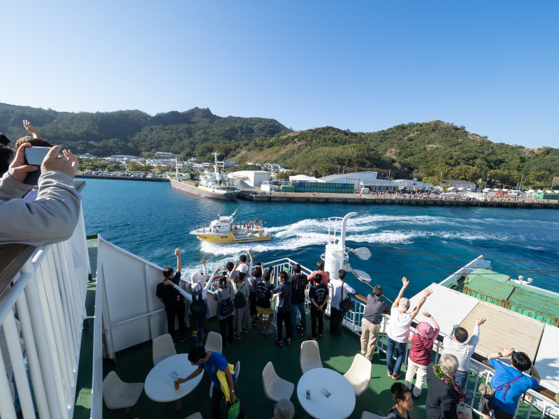 おがさわら丸が港から離れ外海に出るまでのしばらくの間、小舟による見送りの伴走が続く。何隻もの船の上から手を振り続けてくれる人々の姿に、思わず島に滞在していた時間を振り返る。<br>OLYMPUS OM-D E-M5 Mark III / M.ZUIKO DIGITAL ED 7-14mm F2.8 PRO / 7mm / 絞り優先AE（F8・1/250秒・+0.3EV） / ISO 200
