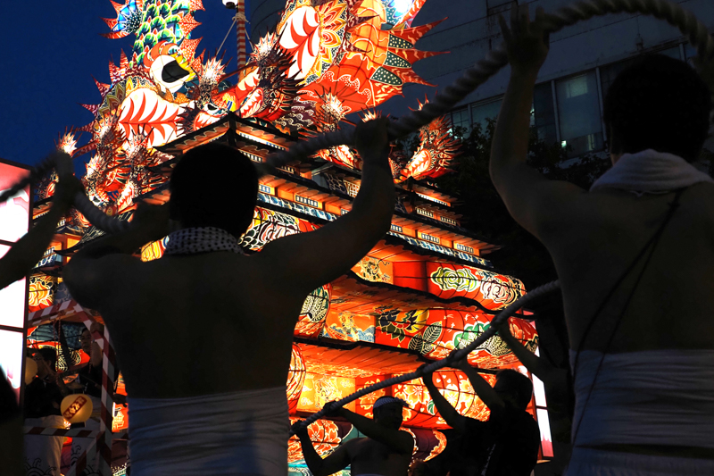 伝統行事「能代役七夕」。男衆が巨大な城郭灯籠を引きながら街を練り歩く。幅広い焦点域をカバーし、小型・軽量設計である本レンズは、機動力が求められる撮影で威力を発揮する（撮影：高橋智史）。<br><span class="fnt-85">OLYMPUS OM-D E-M1X / M.ZUIKO DIGITAL ED 12-200mm F3.5-6.3 / 25mm（50mm相当） / 絞り優先AE（F4.7、1/125秒、-1.3EV） / ISO 1000 / WB：オート</span>