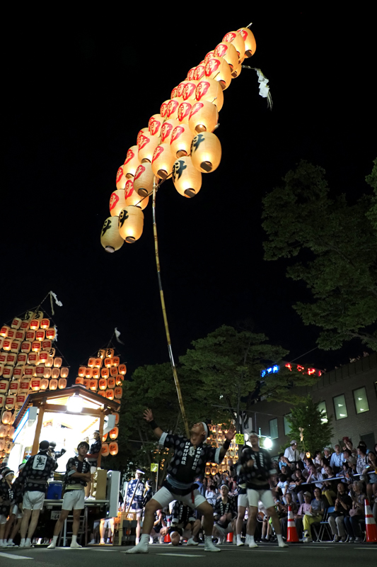 五穀豊穣を祈願する国重要無形民俗文化財「秋田竿燈まつり」。「光の稲穂」と形容される約280本の竿燈が夜空を彩り、演技者は継承されてきた竿燈妙技を披露する。機材の機動力をいかして、演技者に随伴しながら躍動を捉えた（撮影：高橋智史）。<br><span class="fnt-85">OLYMPUS OM-D E-M1X / M.ZUIKO DIGITAL ED 12-200mm F3.5-6.3 / 12mm（24mm相当） / 絞り優先AE（F4、1/15秒、-1.0EV） / ISO 2000 / WB：オート</span>