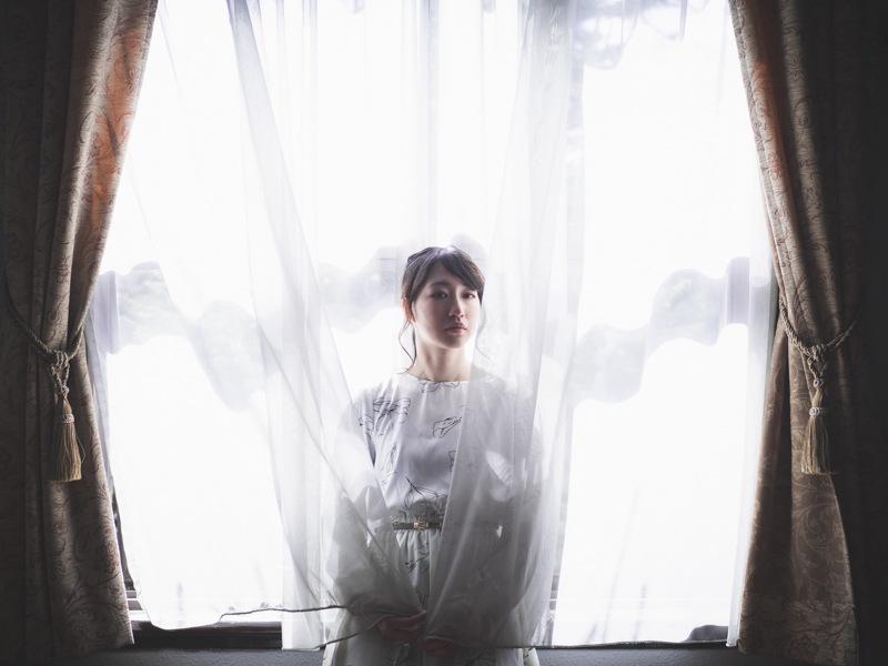 大隈講堂や日比谷公会堂の設計で有名な建築家・佐藤功一が設計した、国の有形文化財である岩手県公会堂。カーテン越しの光に包み込まれたモデルを優しく表現するために開放F1.2で撮影。シャープさと柔らかさを両立できた。<br><span class="fnt-85">OM-D E-M1 Mark III / M.ZUIKO DIGITAL ED 25mm F1.2 PRO /25mm（50mm相当） / 絞り優先AE（F1.2、1/1,600秒、+3.0EV） / ISO 200 / WB:オート</span>